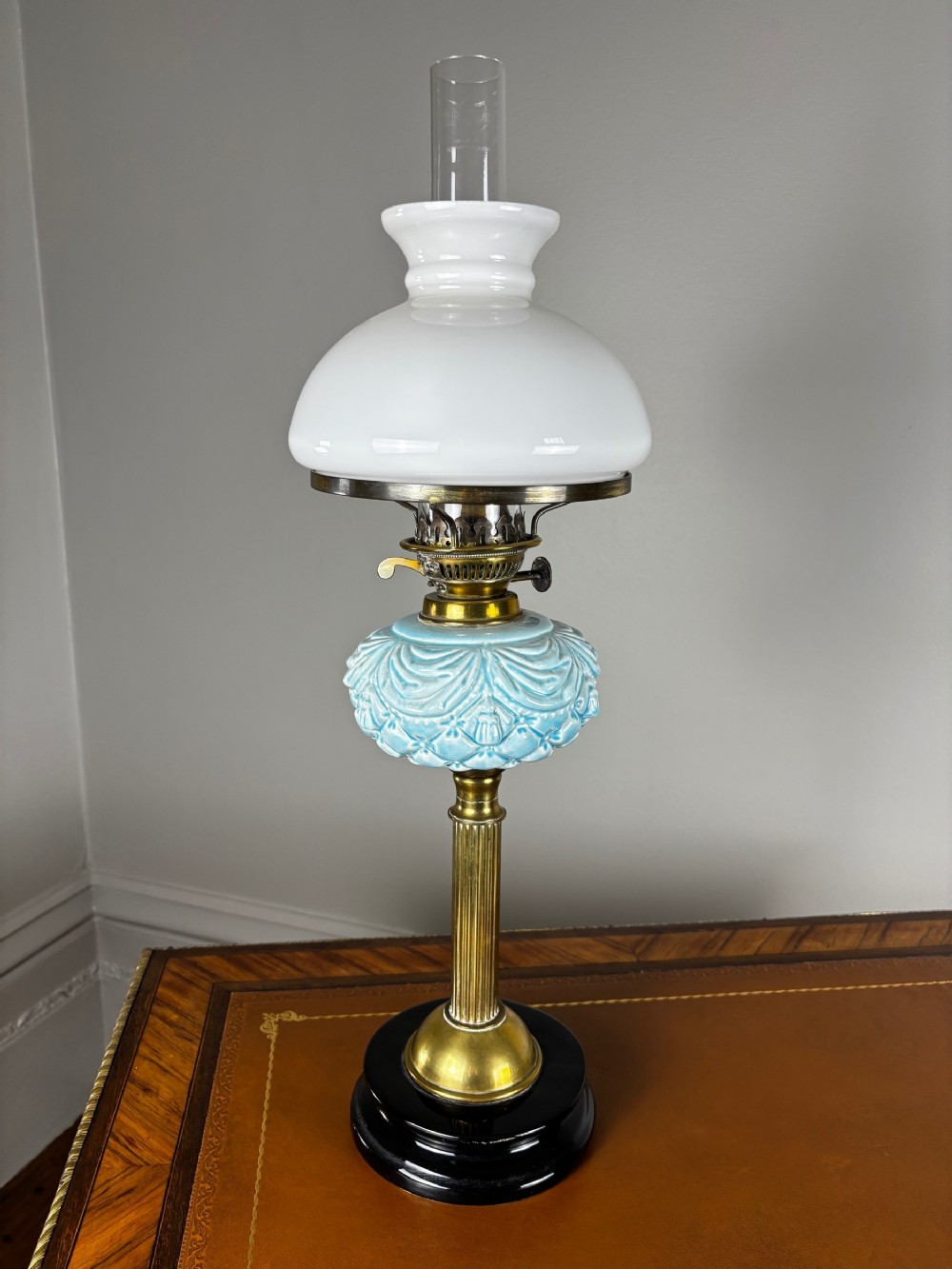 A late Victorian oil lamp featuring a black glass stepped base, a fluted brass column, a light blue moulded ceramic reservoir, and a white glass shade with a clear glass chimney.