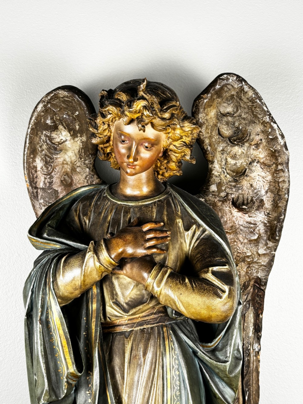 A 19th-century Italian carved wooden angel sculpture featuring extended feathered wings, muted green draped robes, and crossed hands over the chest on a square base. View II