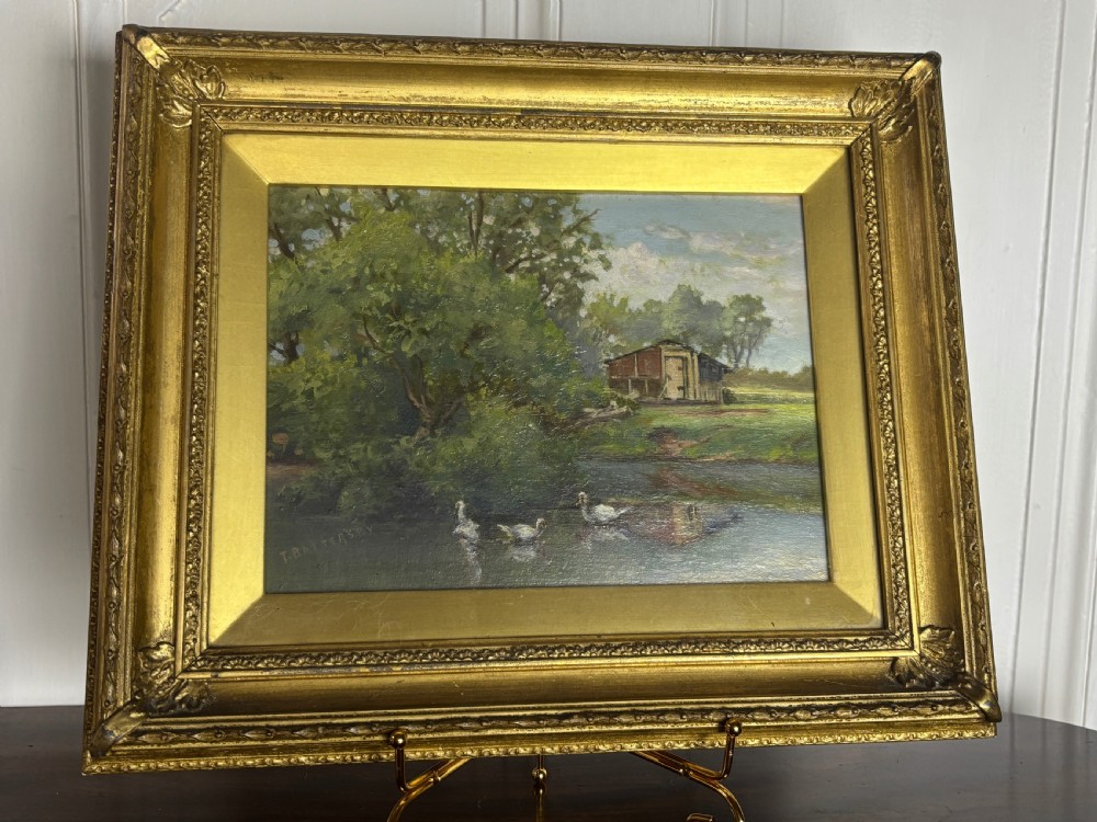 An oil painting on board depicting ducks swimming on a pond beside trees and a wooden shed, presented in a decorative gold gilt frame.