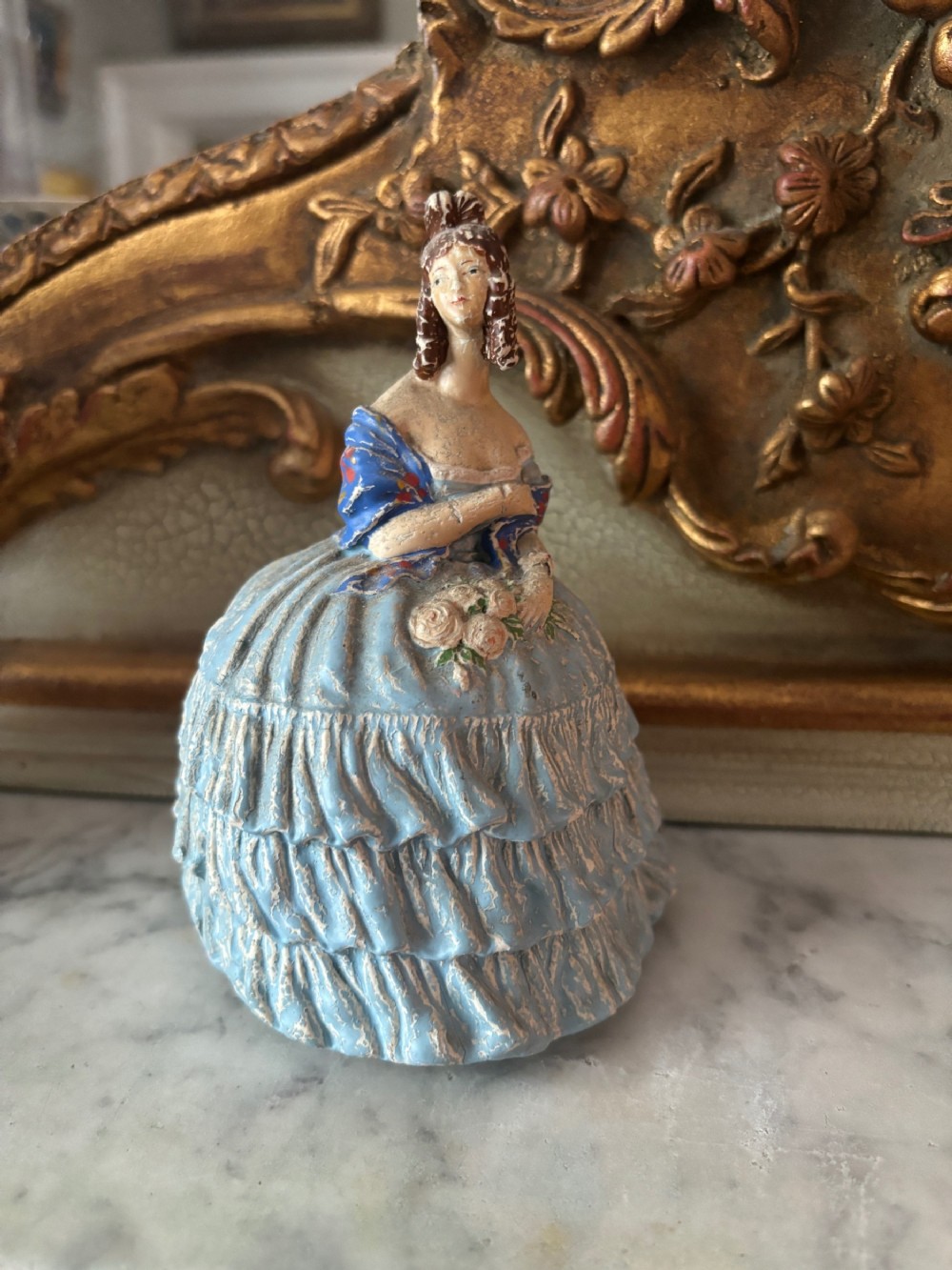 A French papier-mache powder box shaped as a lady in a light blue tiered dress holding a small bouquet of flowers.