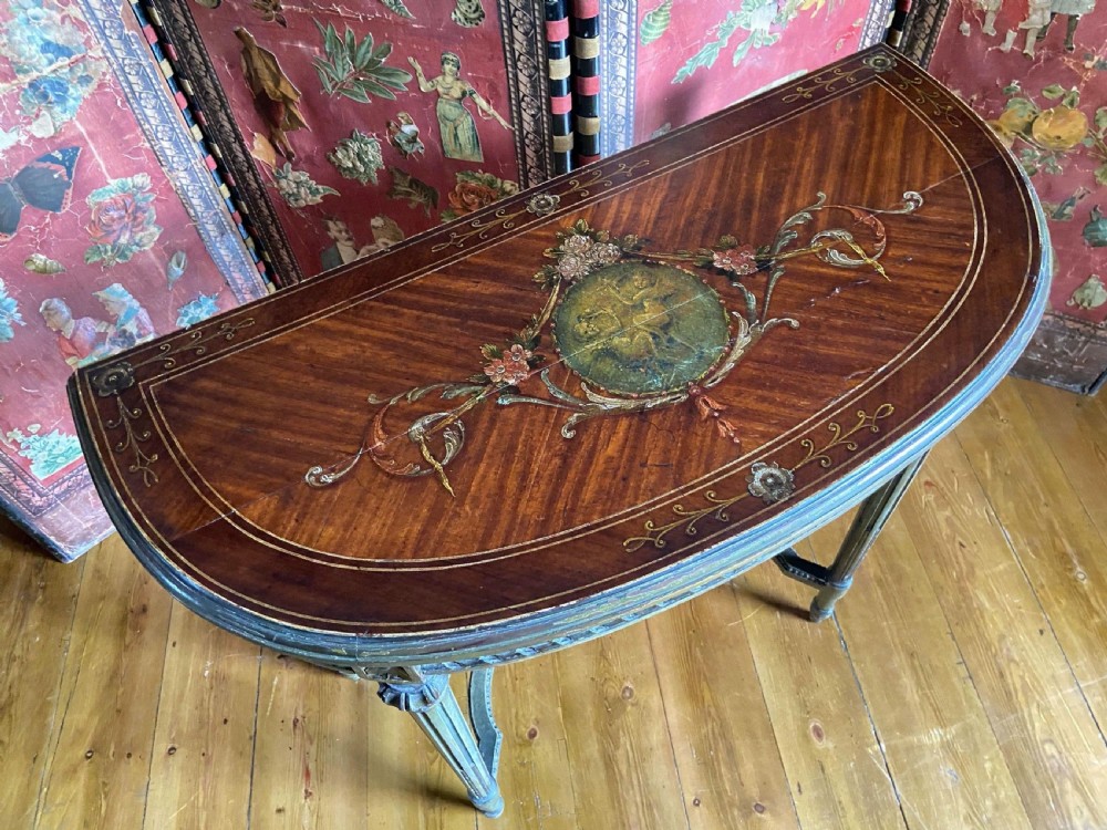 A French demi-lune console table showcasing a semicircular satinwood top decorated with hand-painted floral swags and a central cherub medallion.