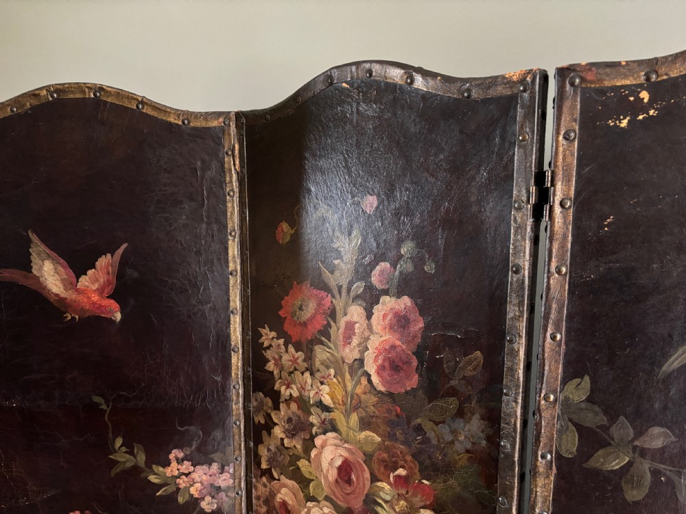 A three-fold dark green leather folding screen decorated with hand-painted floral, fruit, and bird motifs bordered by metal studs. View IV
