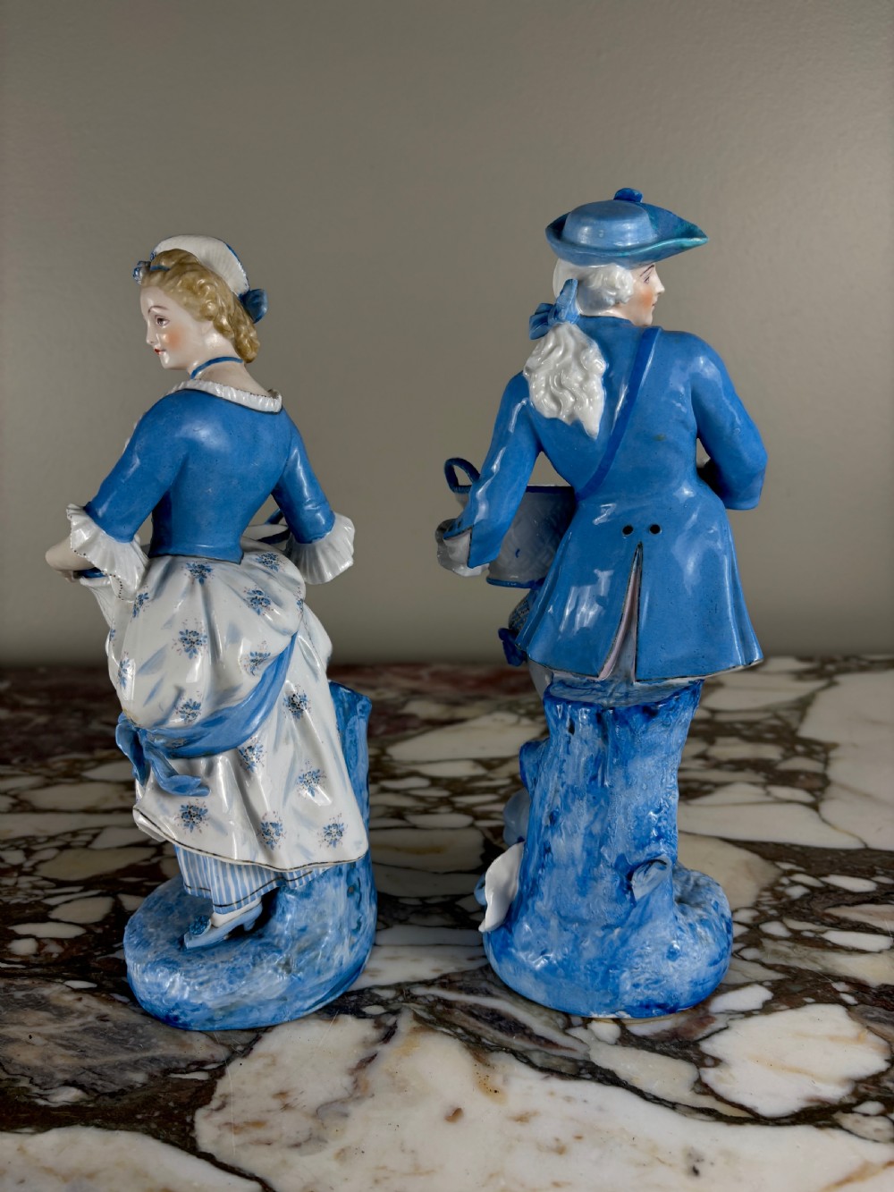 A pair of 19th-century French glazed porcelain figures in blue and white Rococo costume, each holding a woven basket. View VI