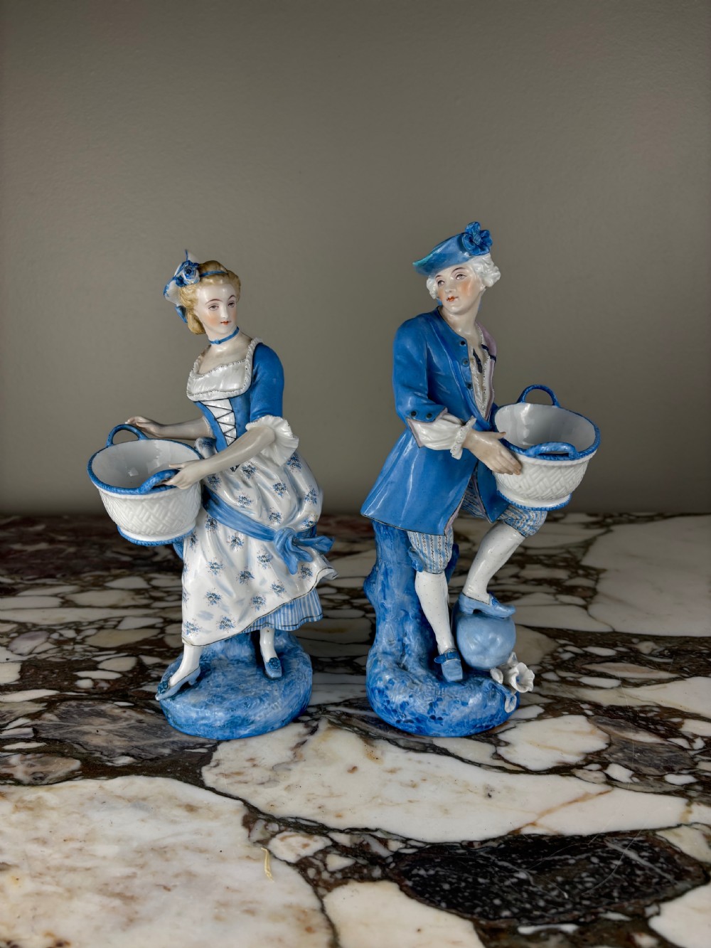 A pair of 19th-century French glazed porcelain figures in blue and white Rococo costume, each holding a woven basket. View XII