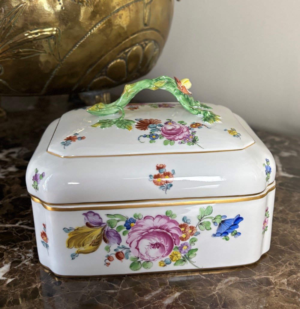 A rectangular white porcelain sugar box decorated with hand-painted flowers, gilded borders, and a green branch handle on the cover.