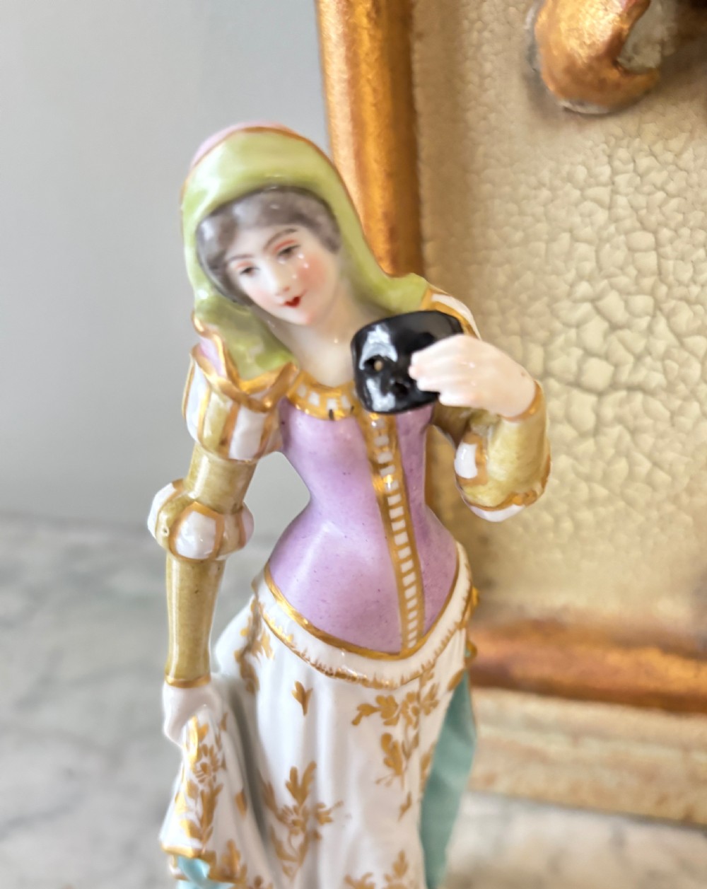 A pair of hand-painted French porcelain figurines depicting an 18th-century man and woman in period costume standing on gilded scroll bases. View X