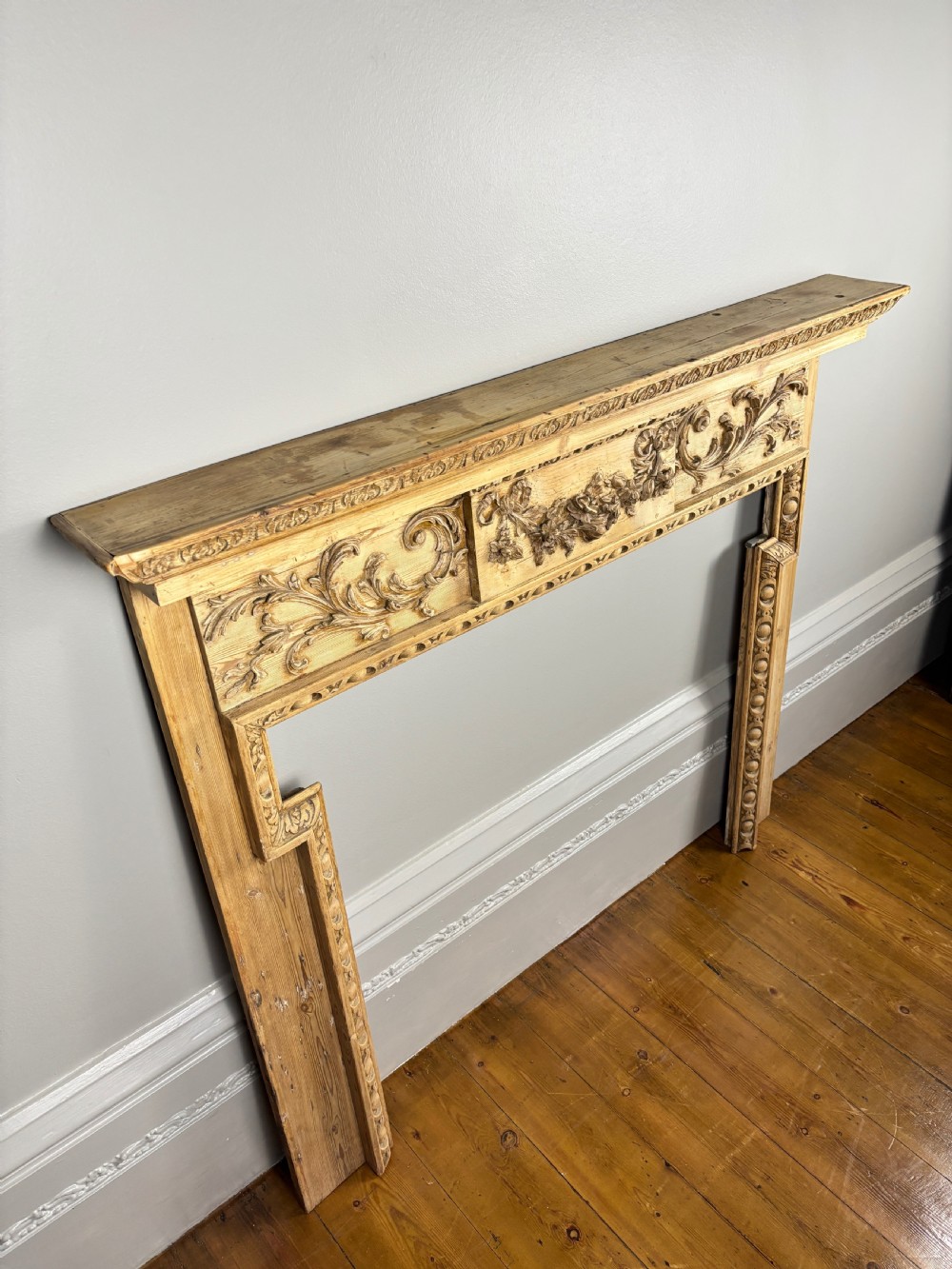 A carved Georgian pine fire surround featuring egg-and-dart moulding, floral swags, and ribbon motifs in a natural timber finish. View II