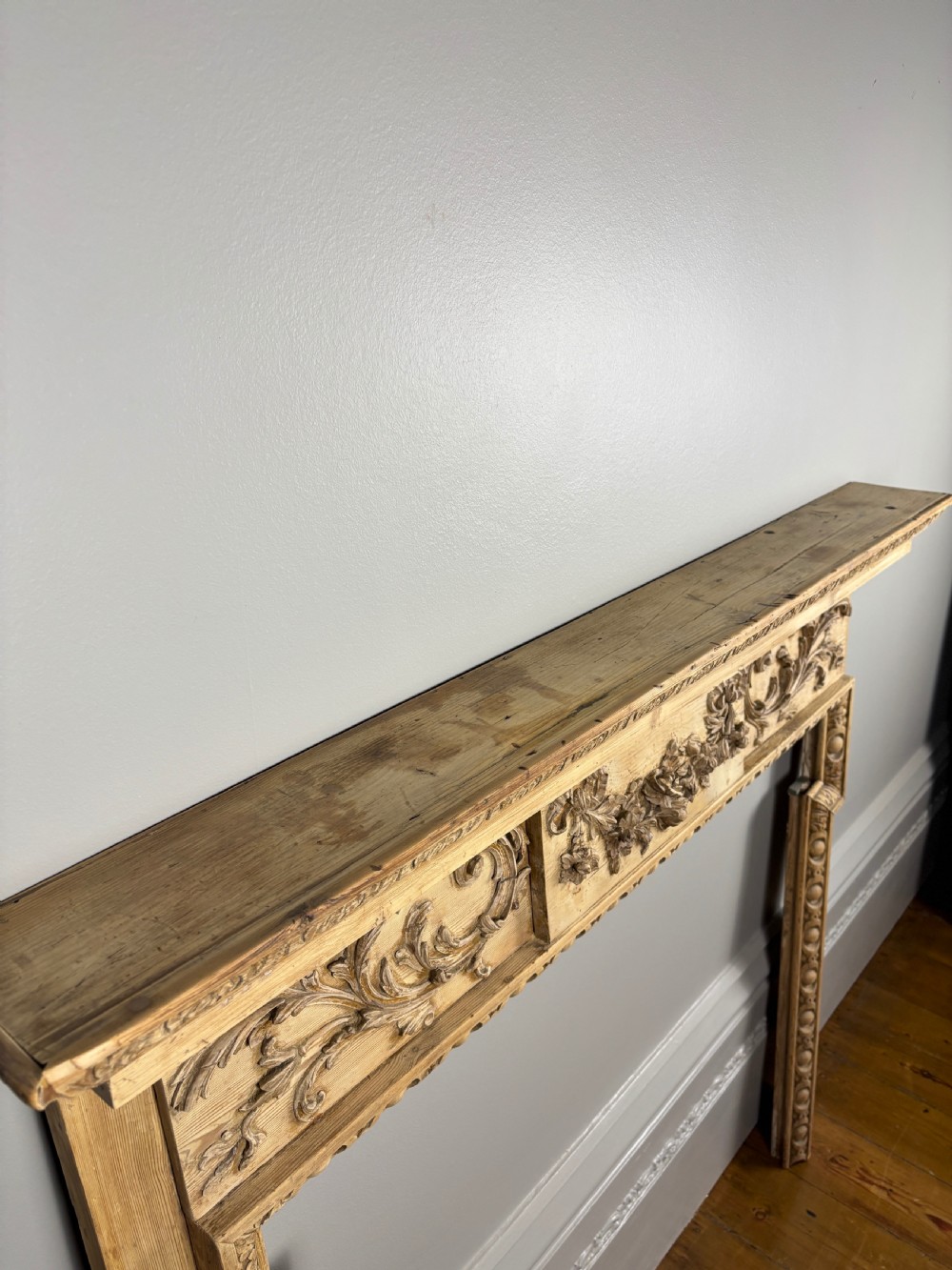 A carved Georgian pine fire surround featuring egg-and-dart moulding, floral swags, and ribbon motifs in a natural timber finish. View IV