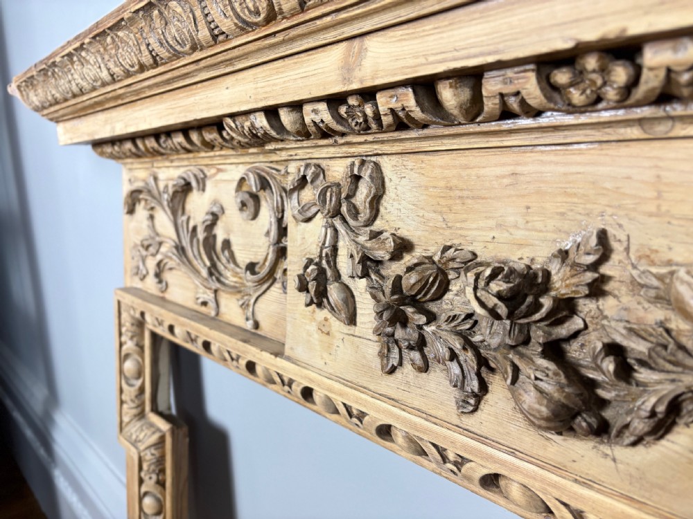 A carved Georgian pine fire surround featuring egg-and-dart moulding, floral swags, and ribbon motifs in a natural timber finish. View VIII