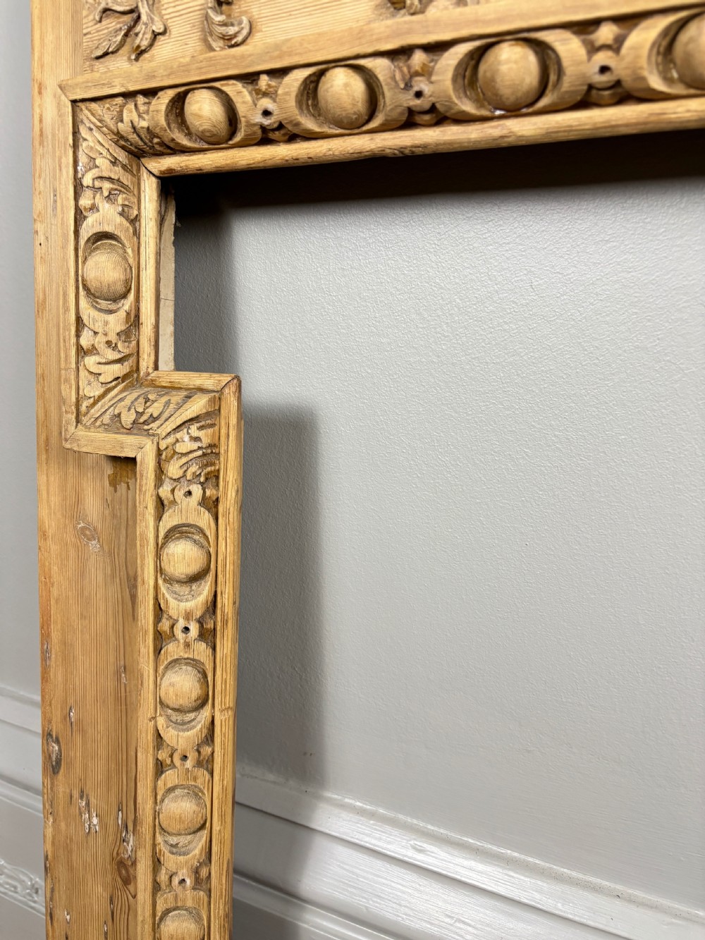 A carved Georgian pine fire surround featuring egg-and-dart moulding, floral swags, and ribbon motifs in a natural timber finish. View IX