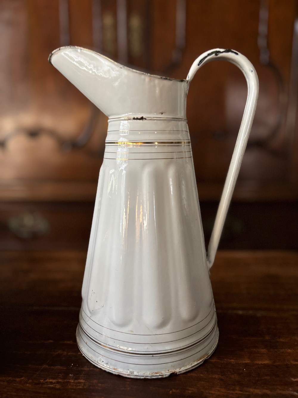 A tall white French enamelware water jug featuring a fluted lower body, thin gold gilt line details, an arched handle, and a raised spout.