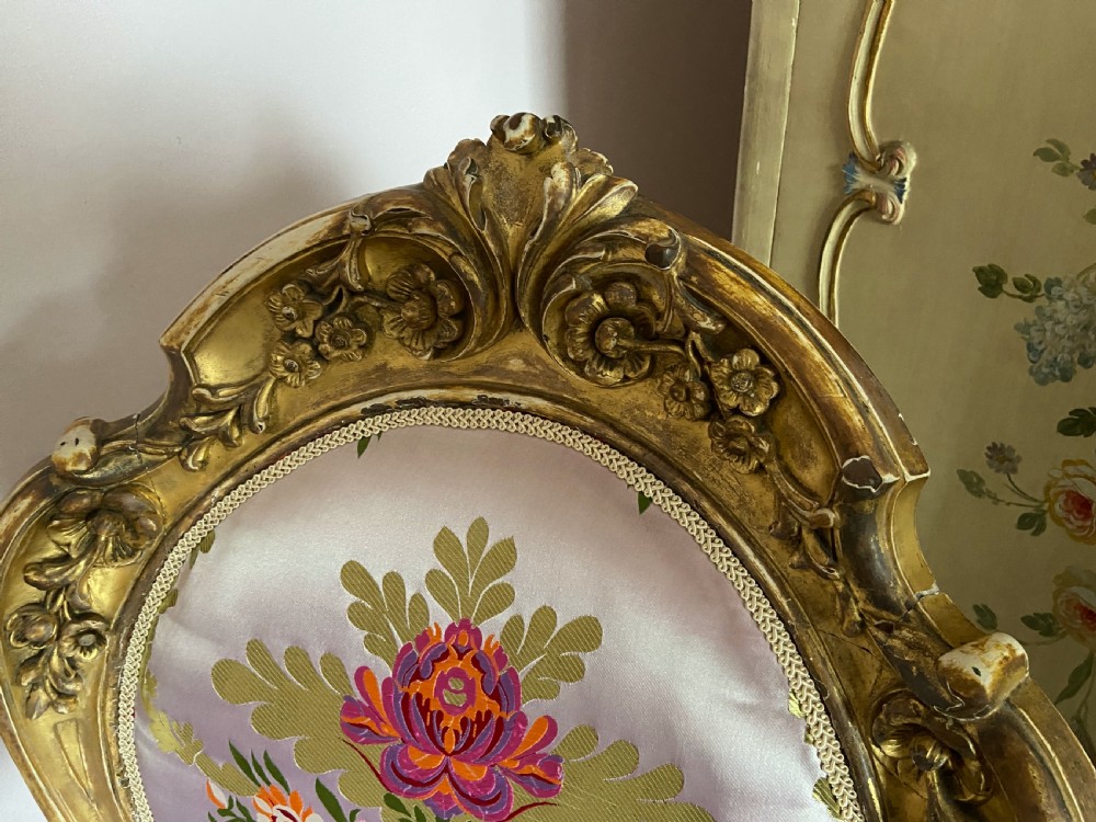 An antique giltwood open armchair with carved scrollwork details, floral silk upholstery, and turned front legs with castors. View III