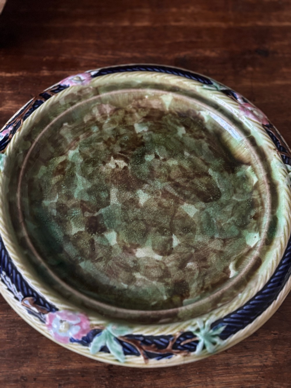 A Victorian majolica cheese dome featuring a cobalt blue glazed body, relief-moulded green leaves, cream rope arches, and pink bows, set on a matching round base. View VI