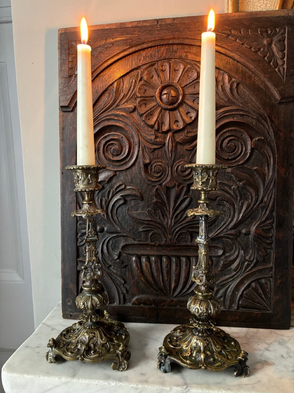 A pair of ornate early 19th-century Regency cast brass candlesticks featuring detailed scrollwork, floral motifs, and shaped bases.