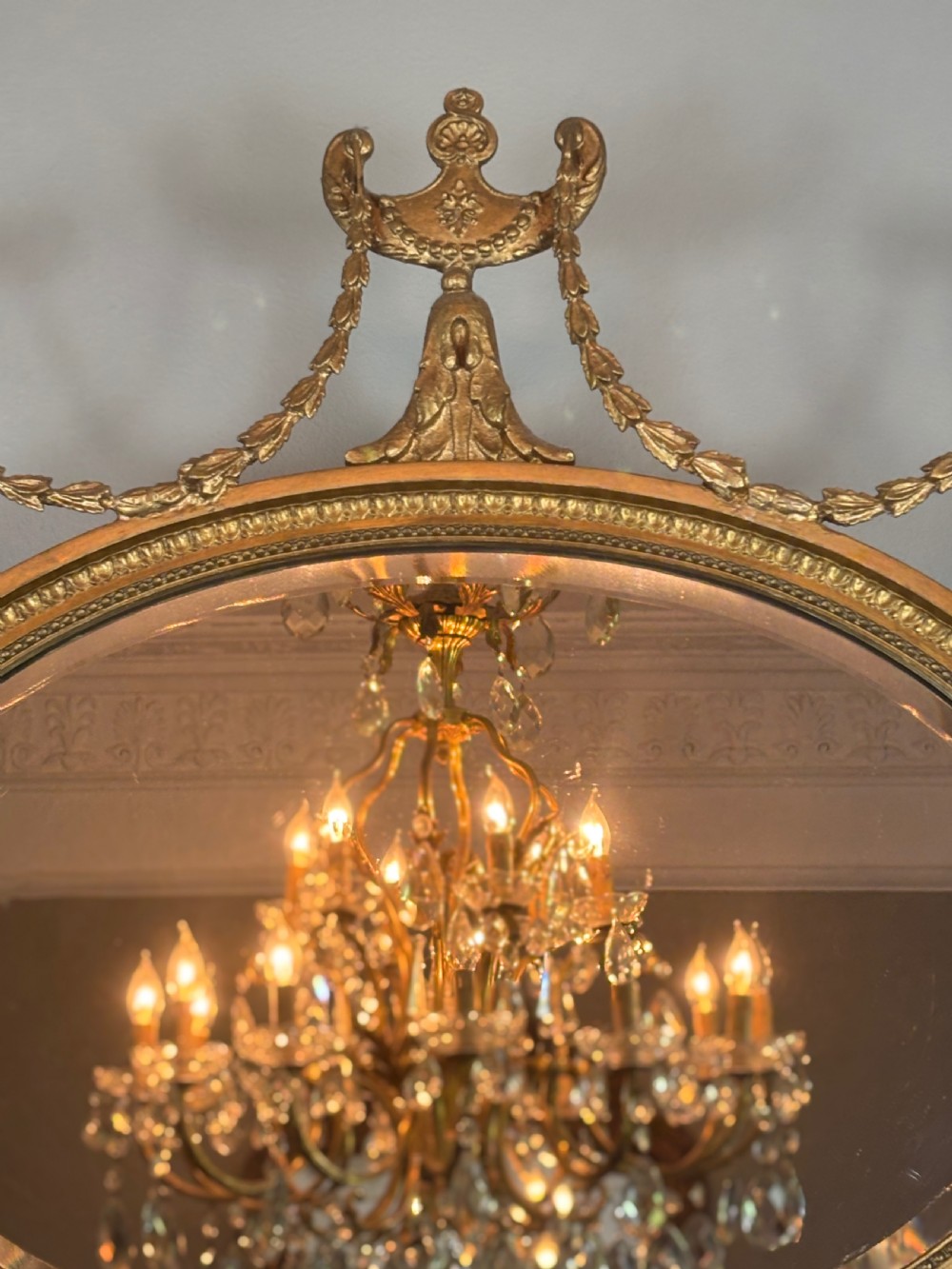 An oval gold giltwood wall mirror featuring a top urn cresting, ribbon bow accents, draped husk garlands, and an inner beaded rim. View IV