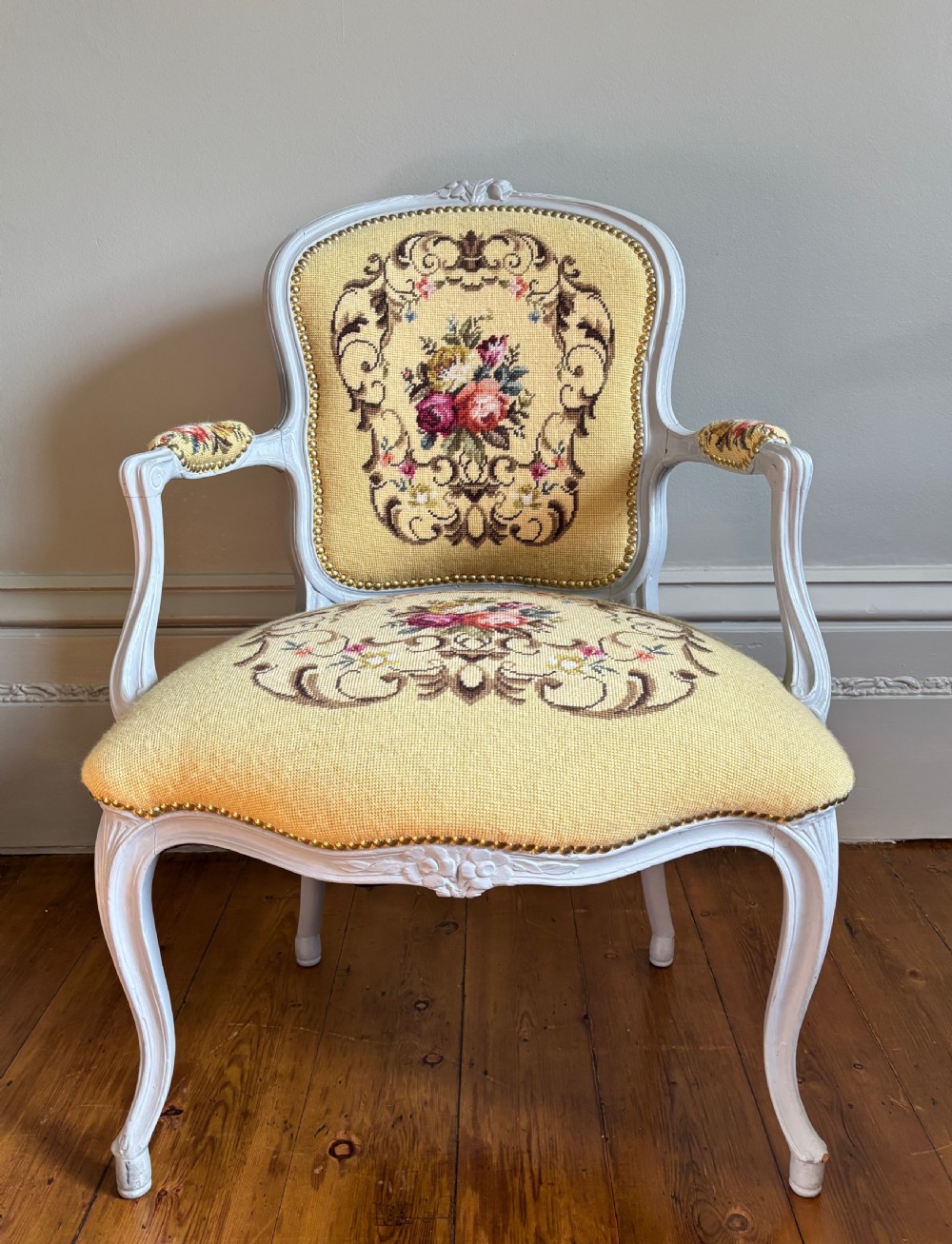 A French Rococo Revival open armchair featuring a grey painted carved frame with yellow floral needlepoint upholstery.