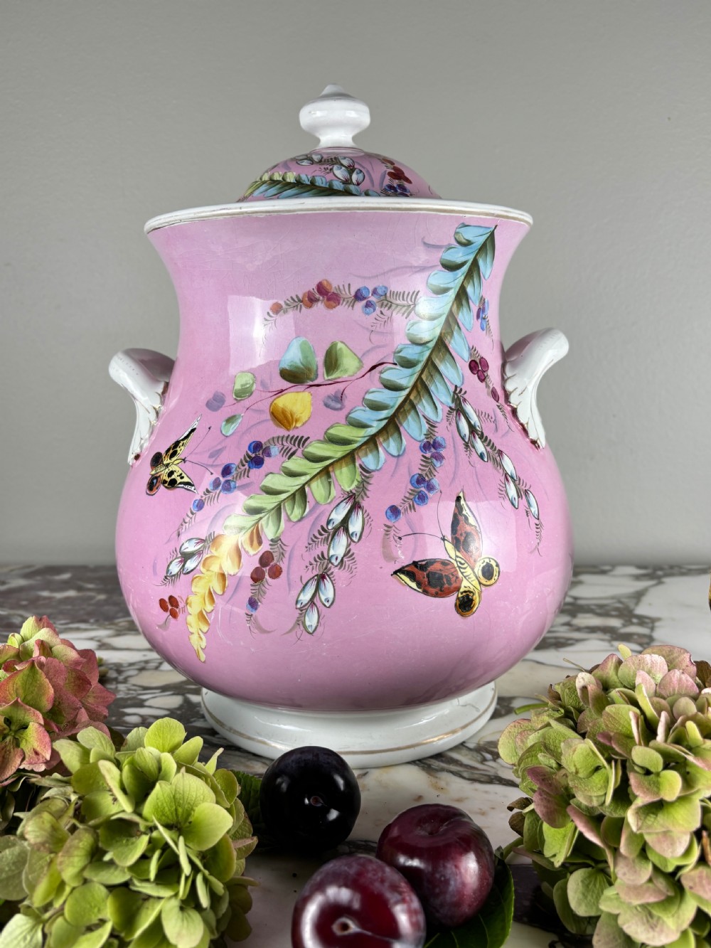 A Victorian Minton ceramic lidded pail featuring hand-painted butterflies and botanical foliage over a pink ground with twin white handles.