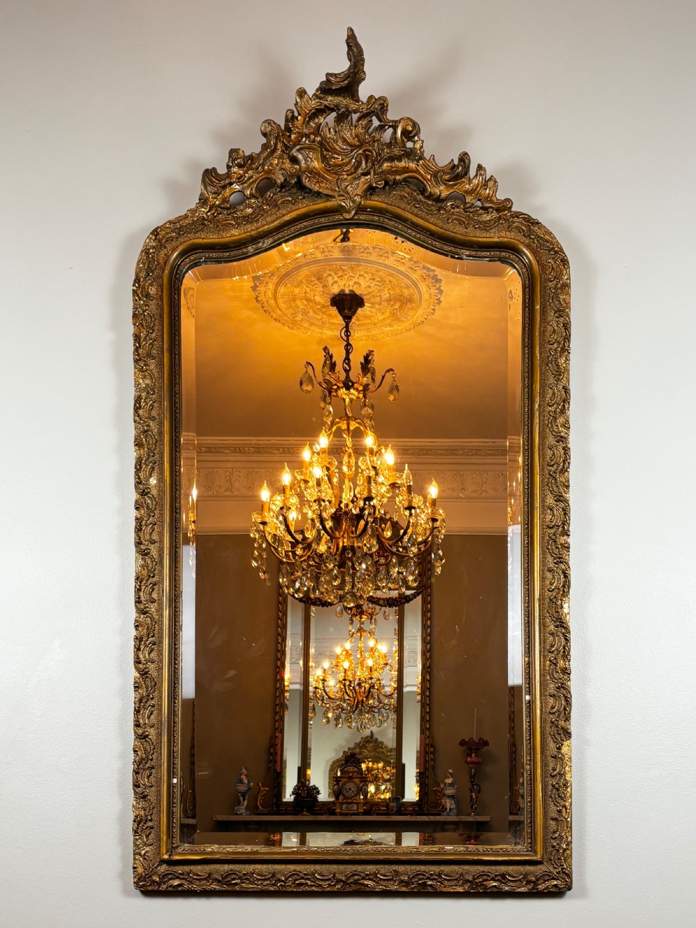 An antique rectangular French Louis Philippe giltwood wall mirror featuring rounded upper corners, an ornate carved crest, and a gold leaf frame.