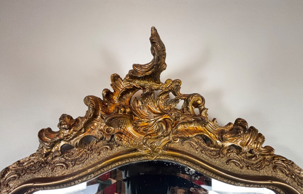 An antique rectangular French Louis Philippe giltwood wall mirror featuring rounded upper corners, an ornate carved crest, and a gold leaf frame. View IV
