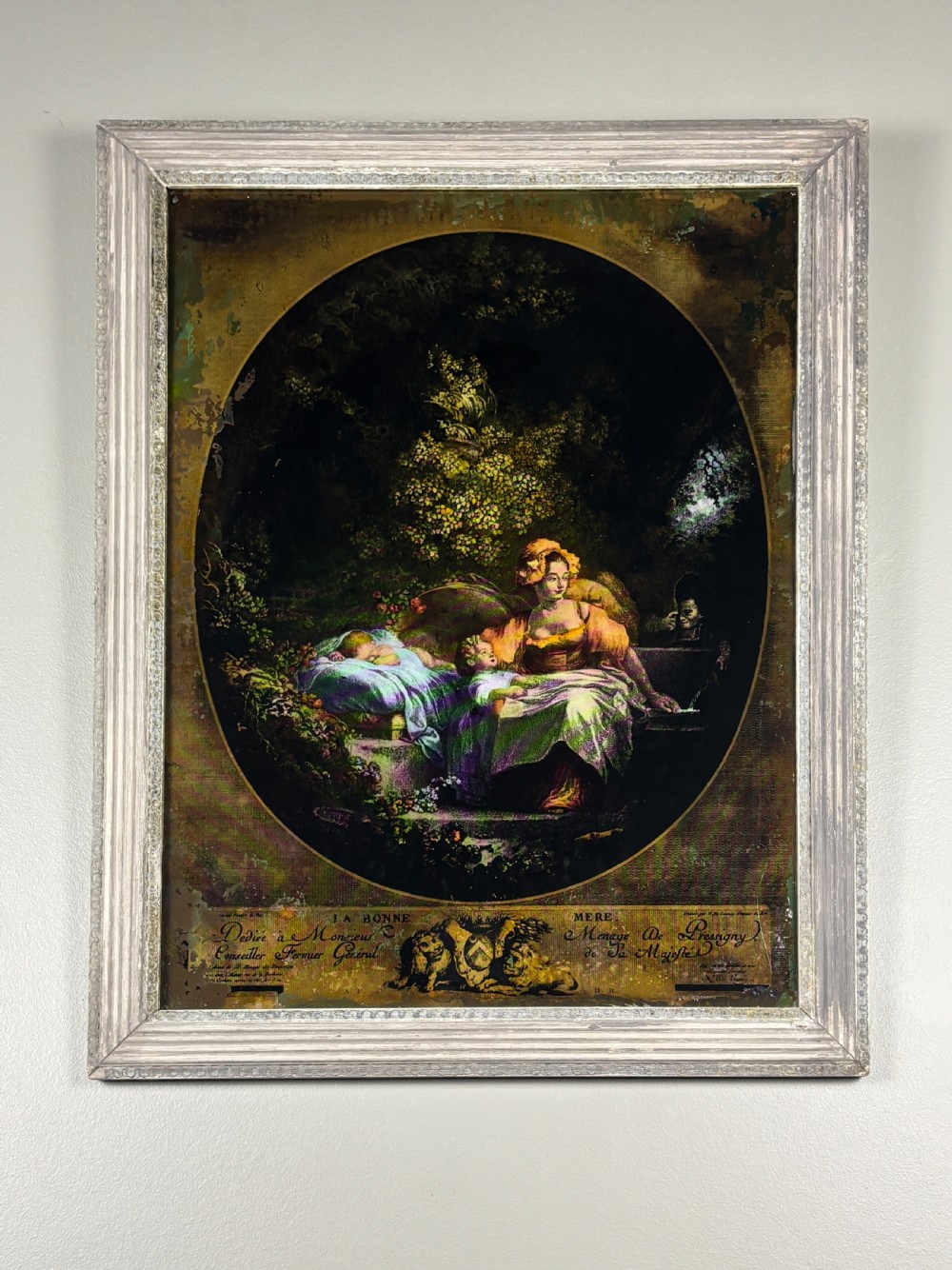 A Georgian reverse print on glass displaying a figure scene inside an oval vignette within a silvered moulded frame.