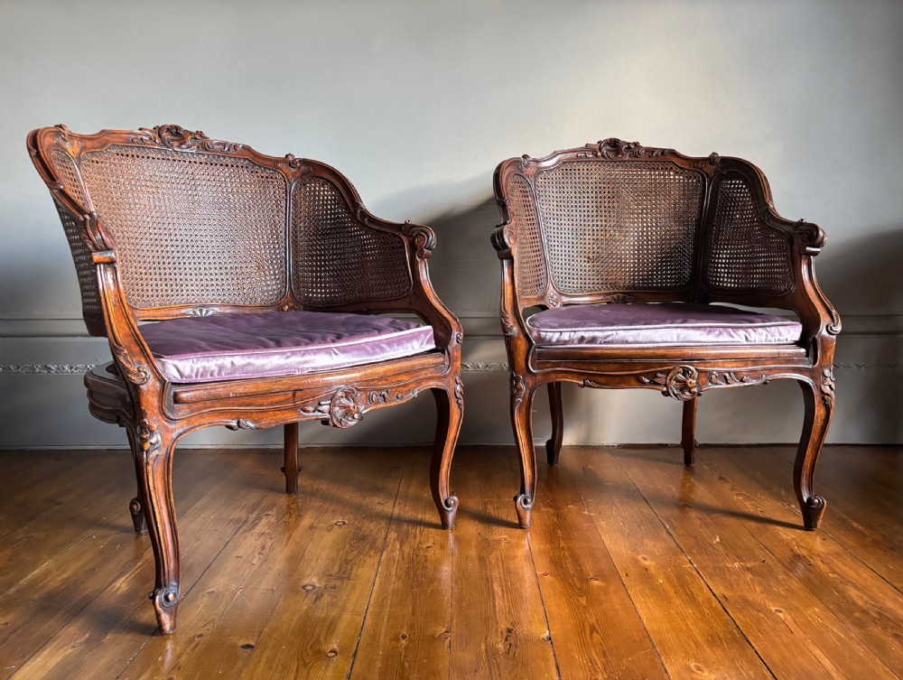 A pair of Louis XV style carved wooden bergere armchairs featuring woven cane backs and purple velvet seat cushions. View II