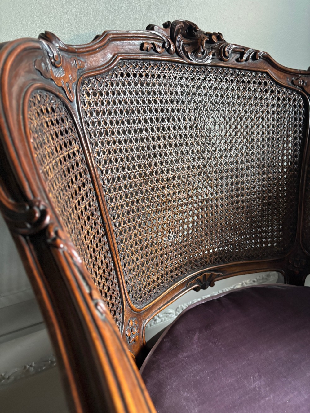 A pair of Louis XV style carved wooden bergere armchairs featuring woven cane backs and purple velvet seat cushions. View IV