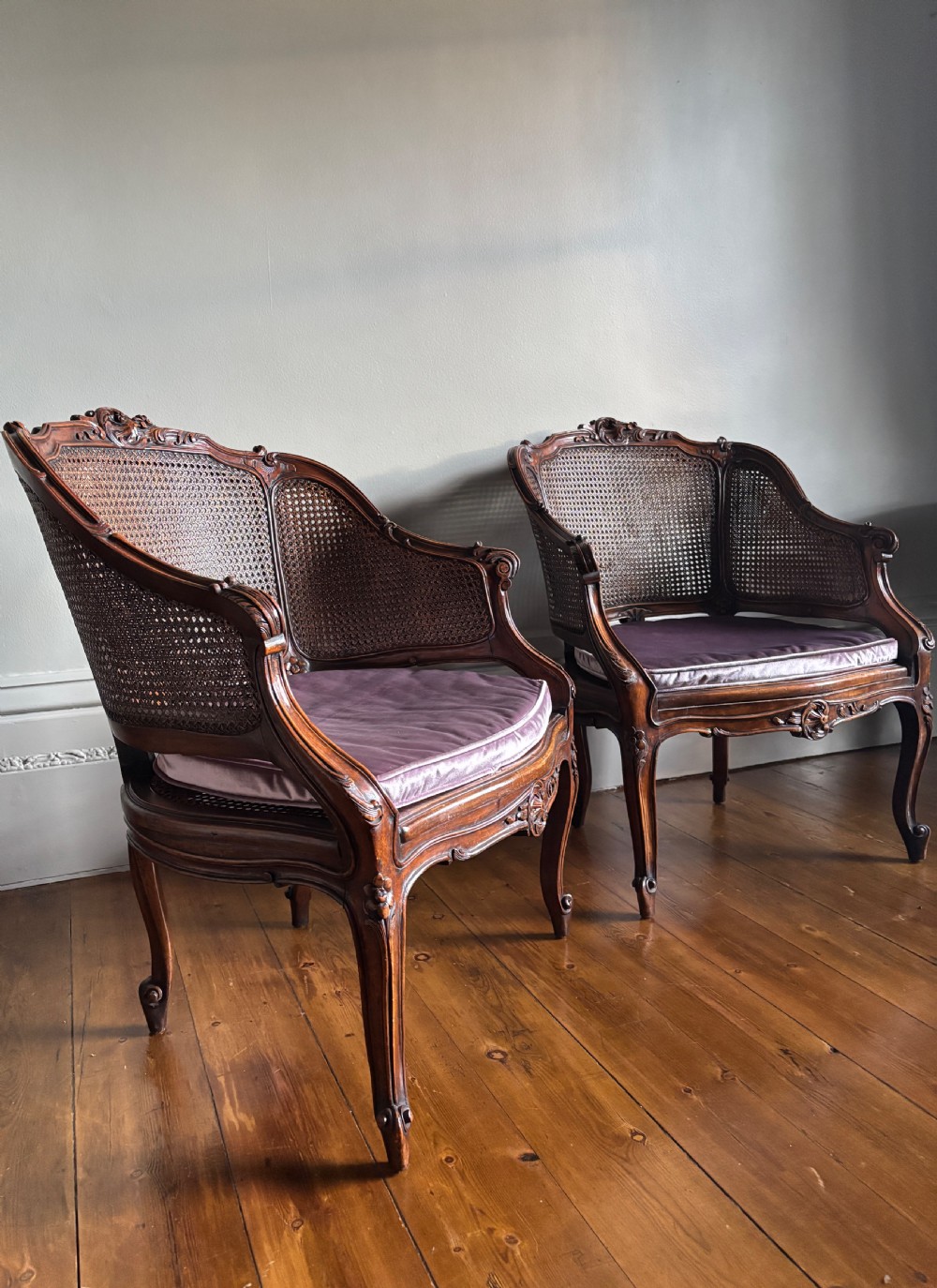A pair of Louis XV style carved wooden bergere armchairs featuring woven cane backs and purple velvet seat cushions. View VII