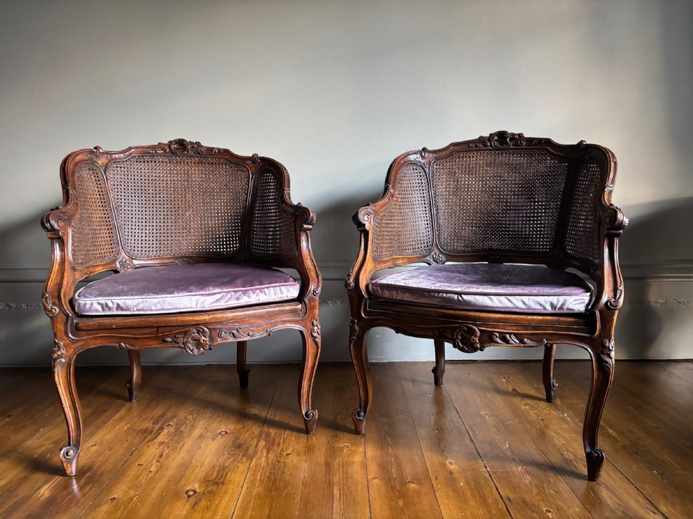 A pair of Louis XV style carved wooden bergere armchairs featuring woven cane backs and purple velvet seat cushions. View X
