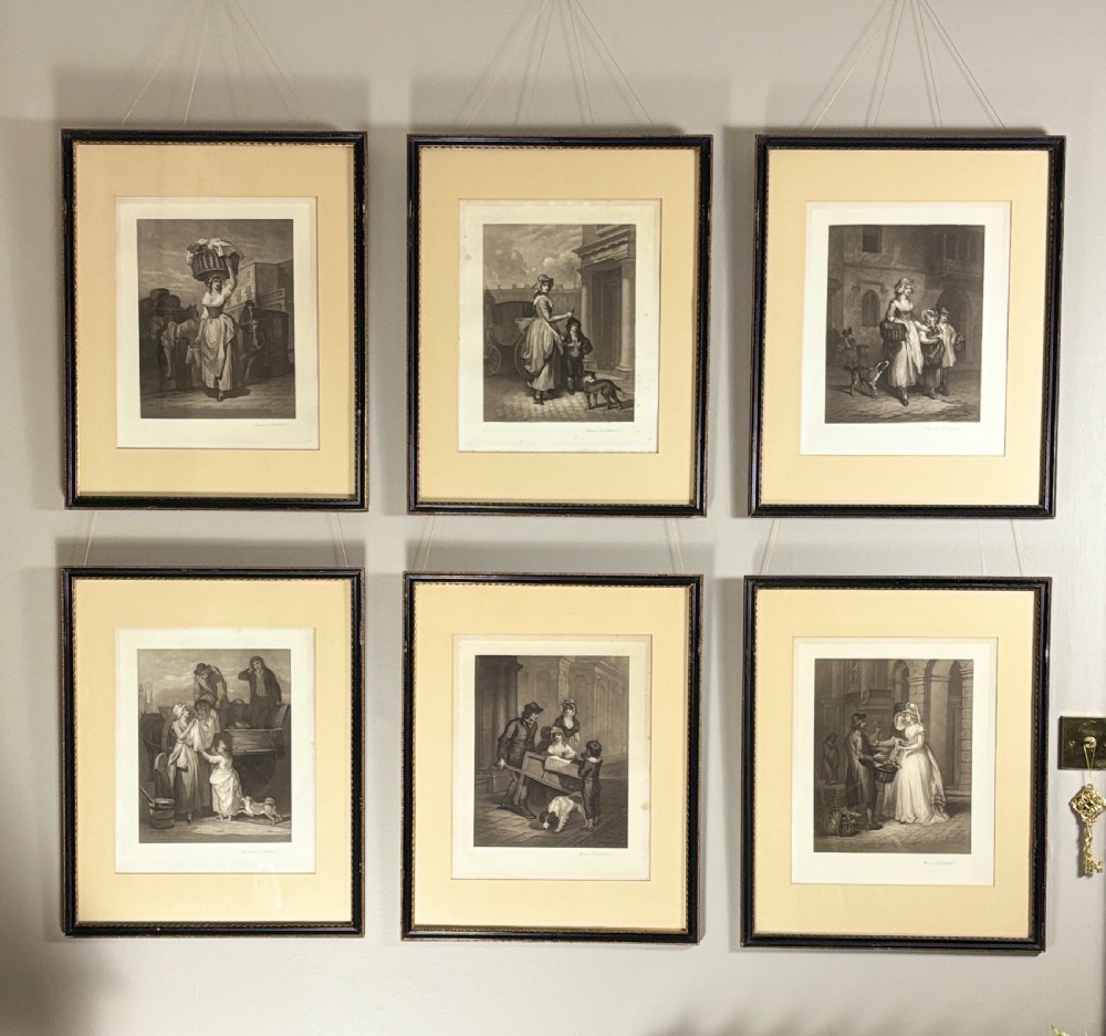 A set of six uniformly framed 19th-century monochrome mezzotint prints depicting figurative street scenes with light cream mounts and dark wood frames. View II