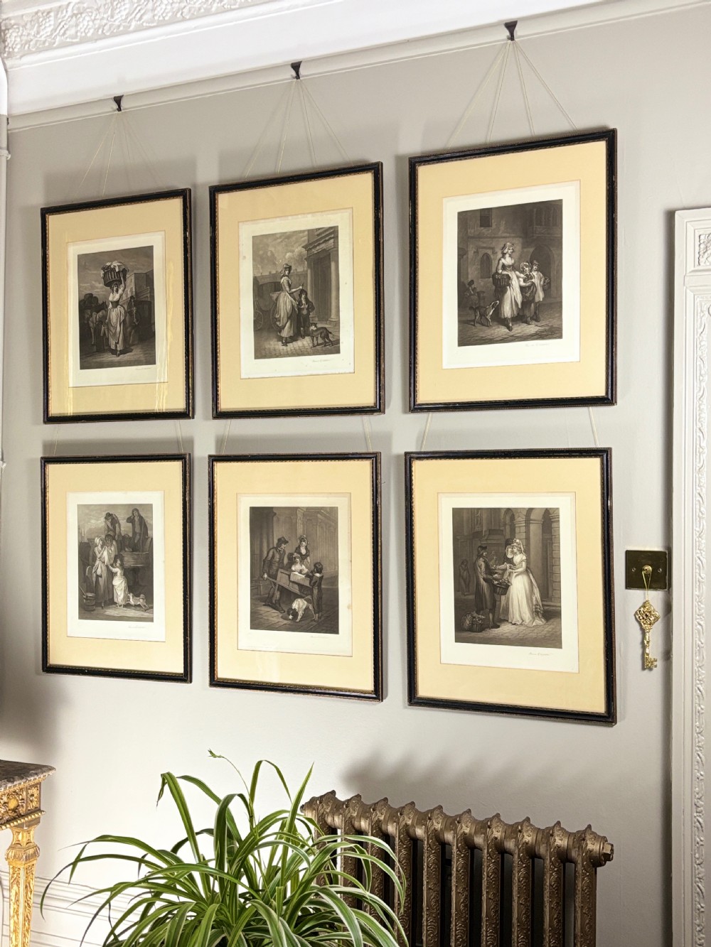 A set of six uniformly framed 19th-century monochrome mezzotint prints depicting figurative street scenes with light cream mounts and dark wood frames.