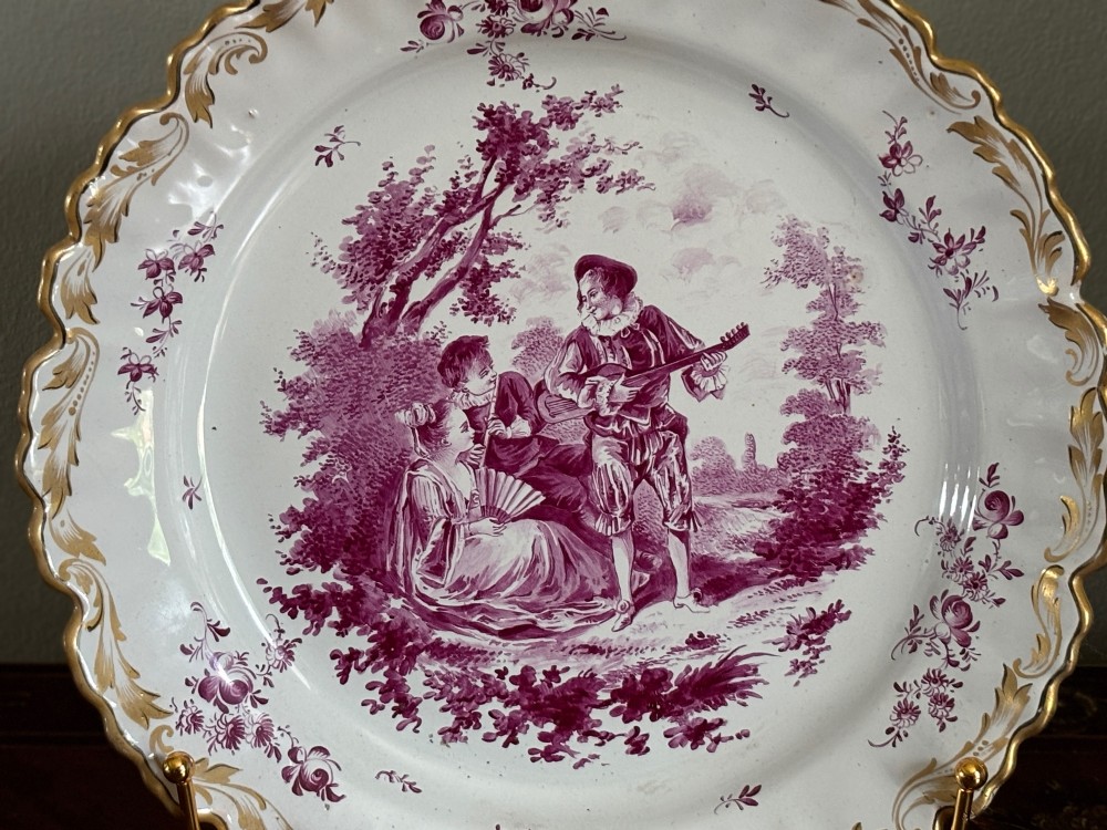 A pair of circular tin-glazed faience dishes featuring central pastoral figures rendered in magenta puce camaieu with gilded scalloped edges. View II