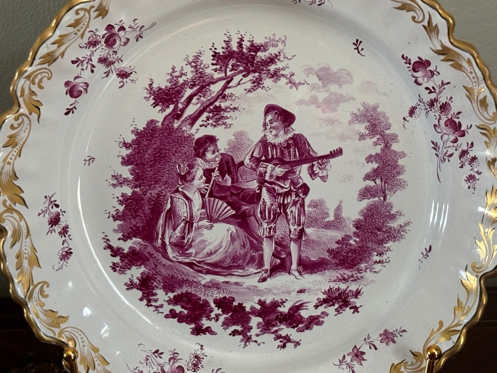 A pair of circular tin-glazed faience dishes featuring central pastoral figures rendered in magenta puce camaieu with gilded scalloped edges. View III