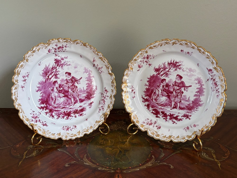 A pair of circular tin-glazed faience dishes featuring central pastoral figures rendered in magenta puce camaieu with gilded scalloped edges. View IV