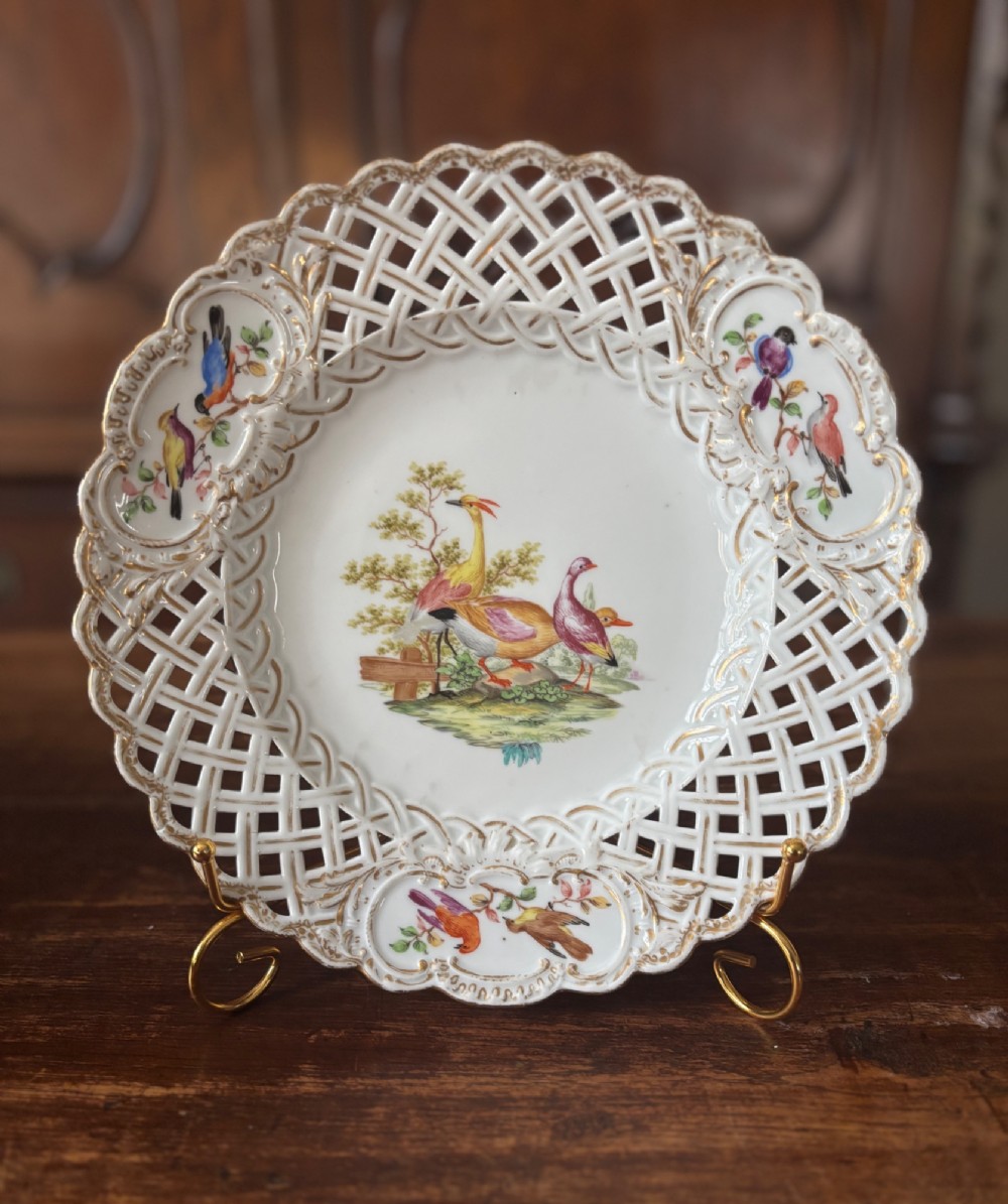 A circular Meissen porcelain cabinet plate featuring a reticulated openwork lattice rim accented with gilded cartouches and hand-painted exotic birds in the centre.