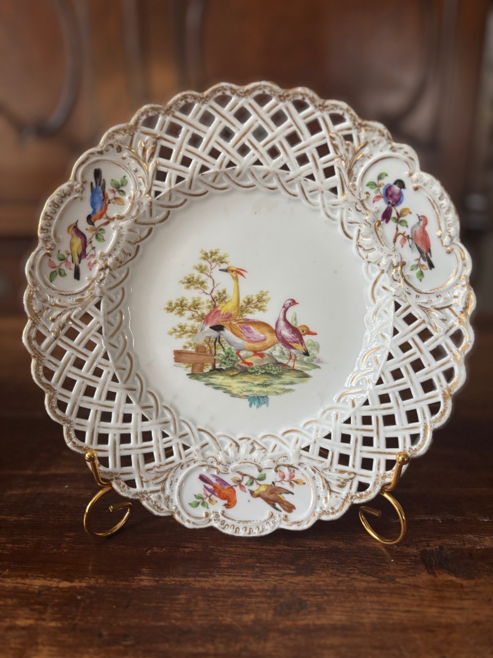 A circular Meissen porcelain cabinet plate featuring a reticulated openwork lattice rim accented with gilded cartouches and hand-painted exotic birds in the centre. View IV