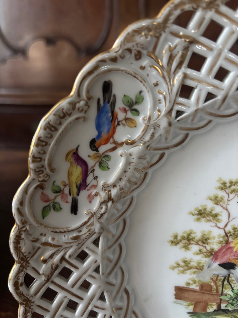 A circular Meissen porcelain cabinet plate featuring a reticulated openwork lattice rim accented with gilded cartouches and hand-painted exotic birds in the centre. View VI