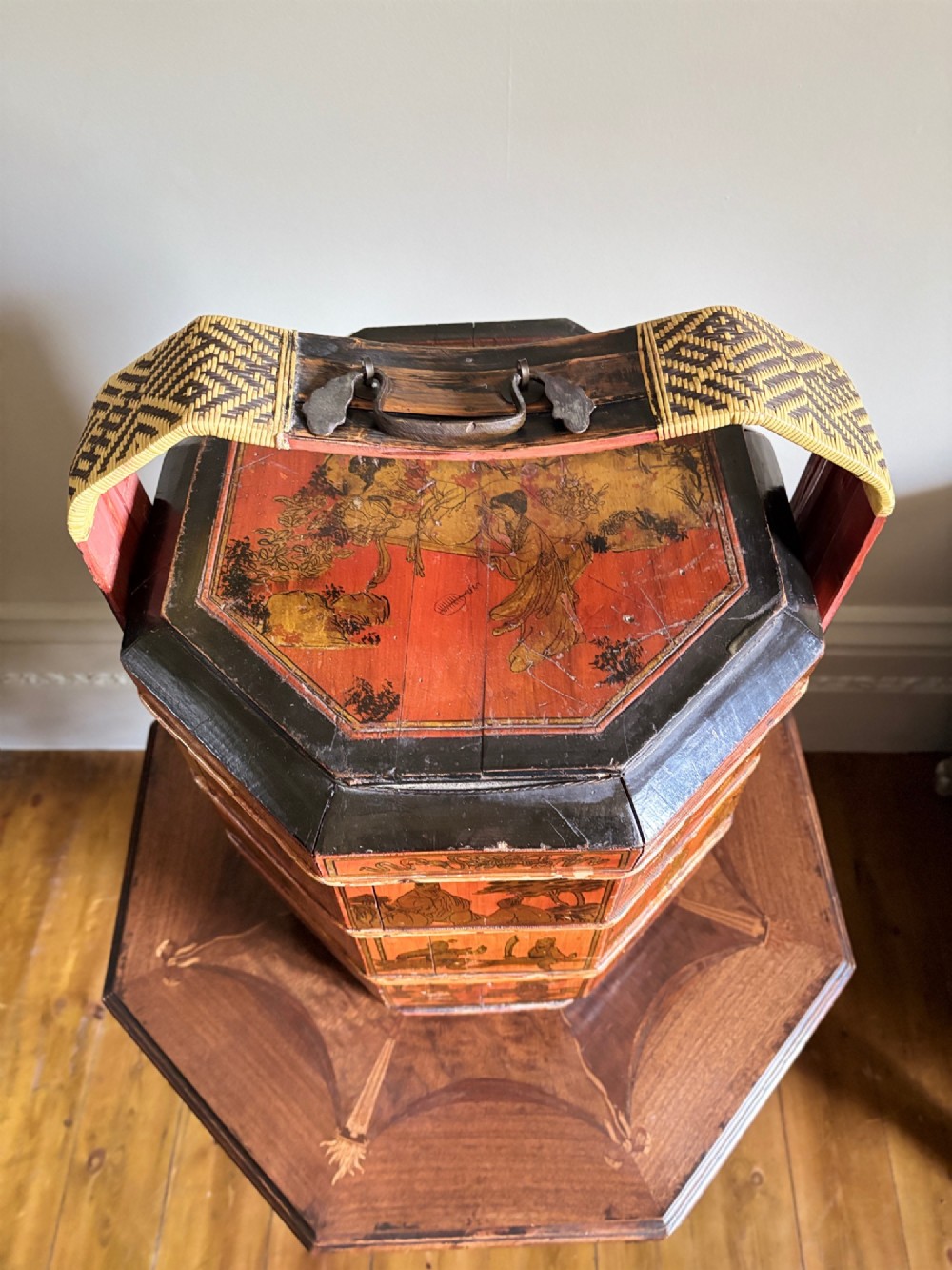 An octagonal red and black lacquered three-tier Chinese dowry basket with an overhead bentwood handle bound in woven cane and panels painted with figures. View III