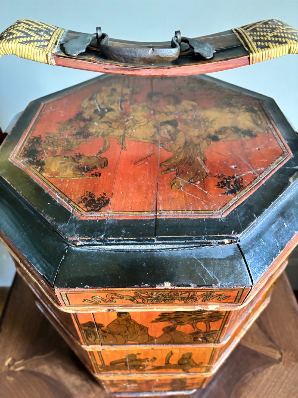 An octagonal red and black lacquered three-tier Chinese dowry basket with an overhead bentwood handle bound in woven cane and panels painted with figures. View IV