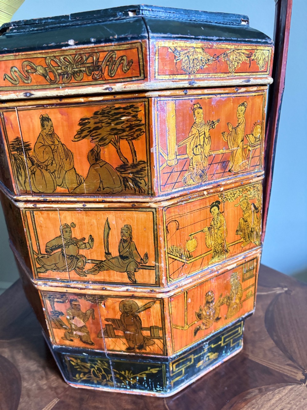 An octagonal red and black lacquered three-tier Chinese dowry basket with an overhead bentwood handle bound in woven cane and panels painted with figures. View VI