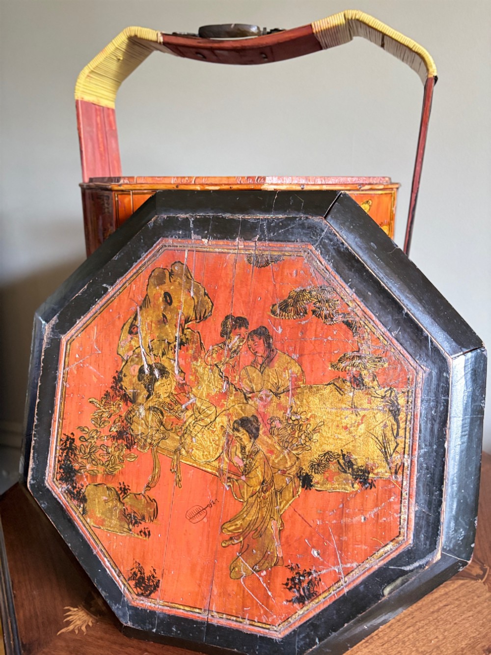 An octagonal red and black lacquered three-tier Chinese dowry basket with an overhead bentwood handle bound in woven cane and panels painted with figures. View IX