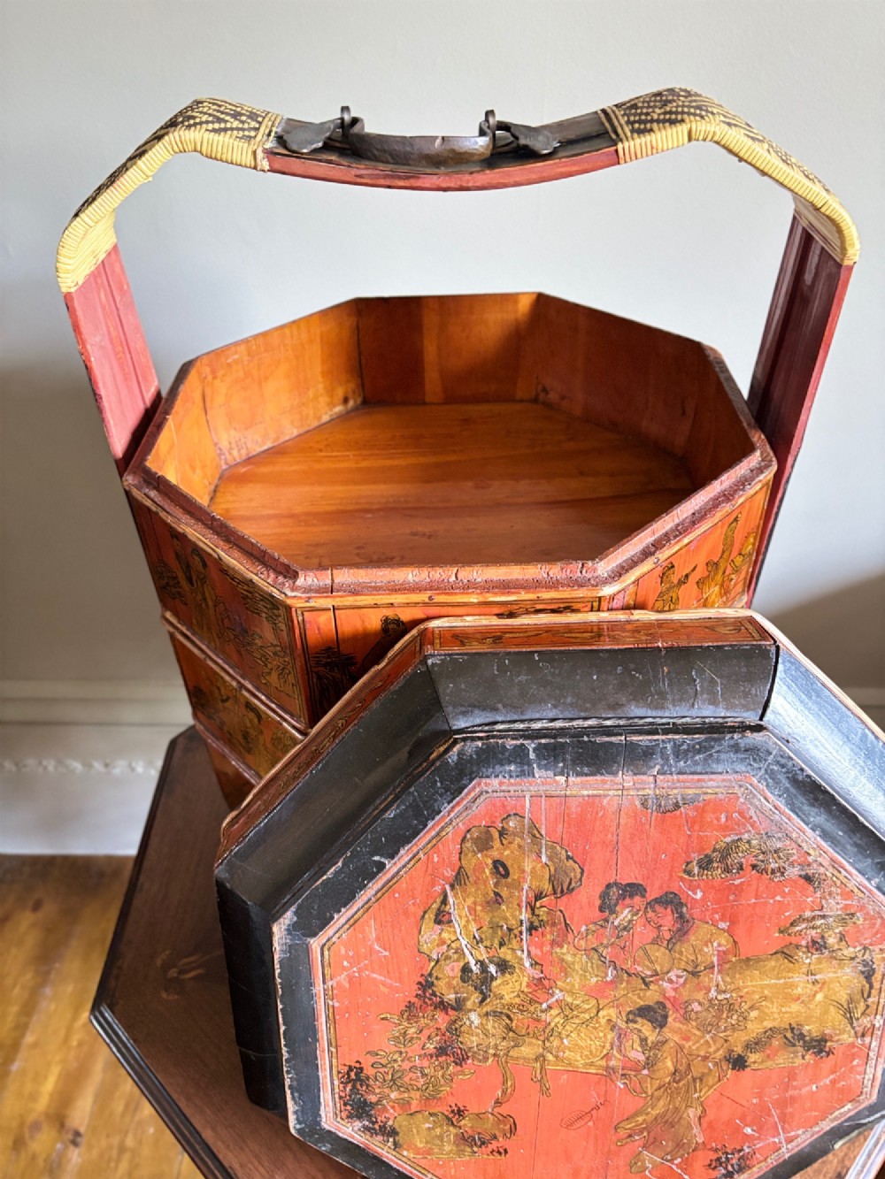 An octagonal red and black lacquered three-tier Chinese dowry basket with an overhead bentwood handle bound in woven cane and panels painted with figures. View X
