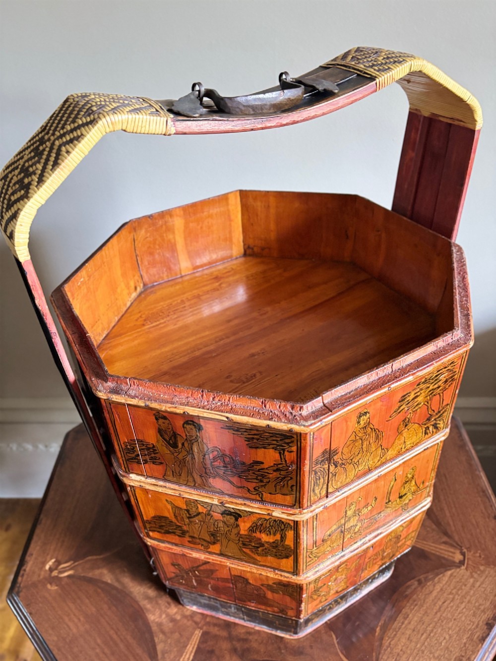 An octagonal red and black lacquered three-tier Chinese dowry basket with an overhead bentwood handle bound in woven cane and panels painted with figures. View XI