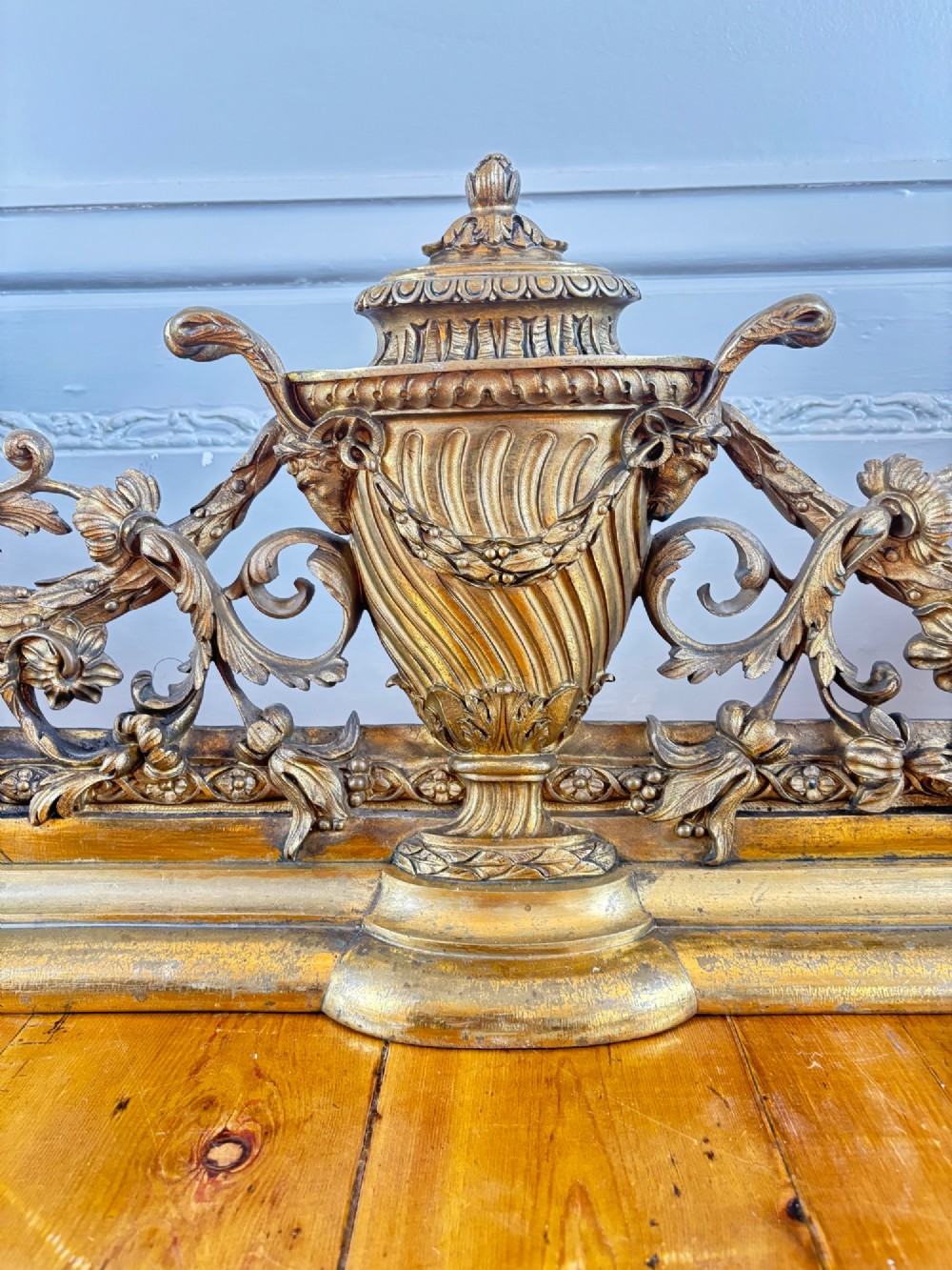 A long gilt bronze fireplace fender featuring winged sphinxes on either side, foliate scrollwork, and a central classical urn on a stepped base. View III