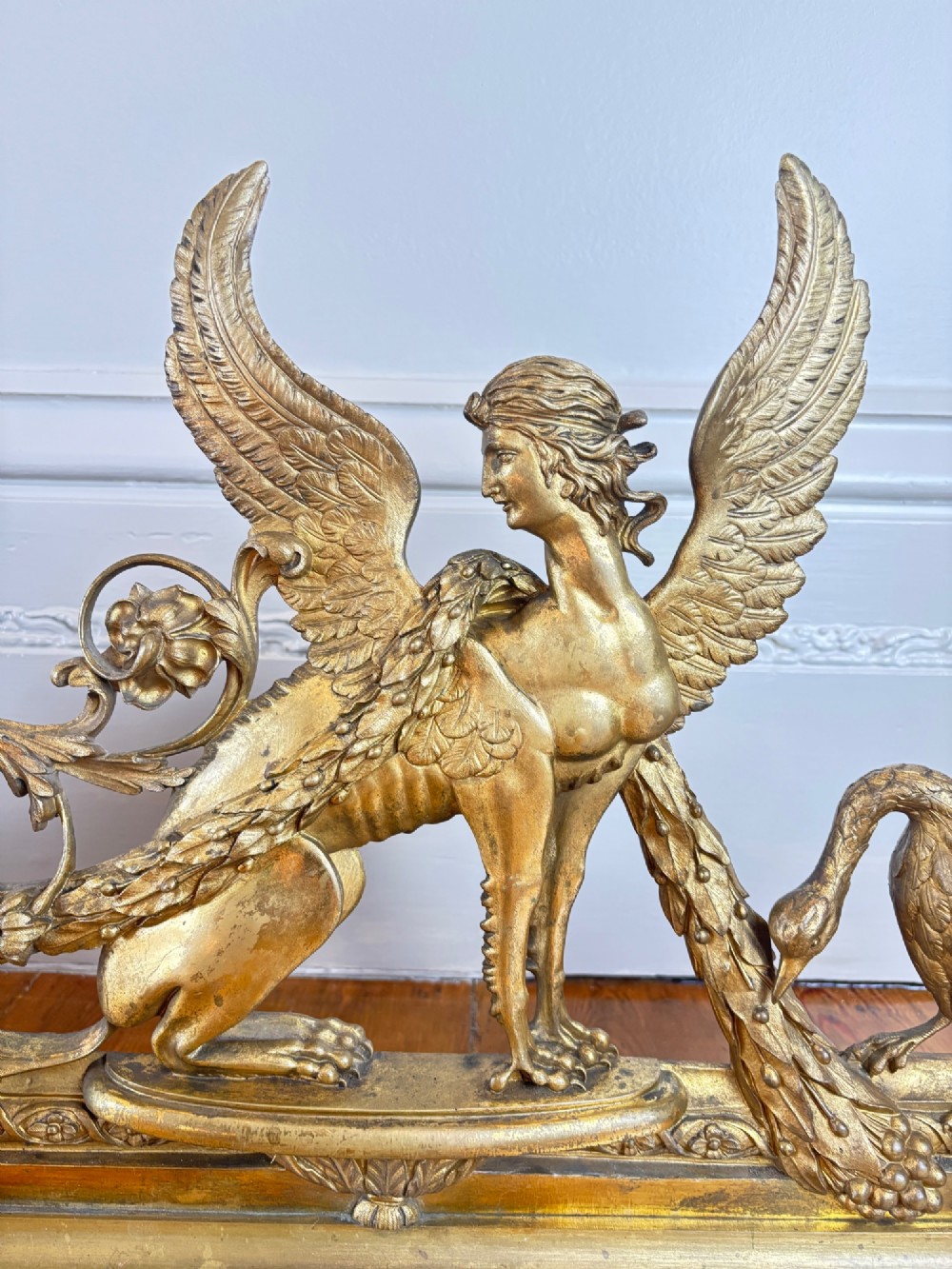 A long gilt bronze fireplace fender featuring winged sphinxes on either side, foliate scrollwork, and a central classical urn on a stepped base. View IV