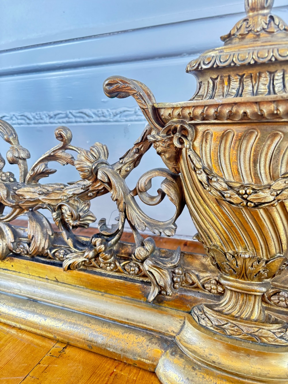 A long gilt bronze fireplace fender featuring winged sphinxes on either side, foliate scrollwork, and a central classical urn on a stepped base. View VI
