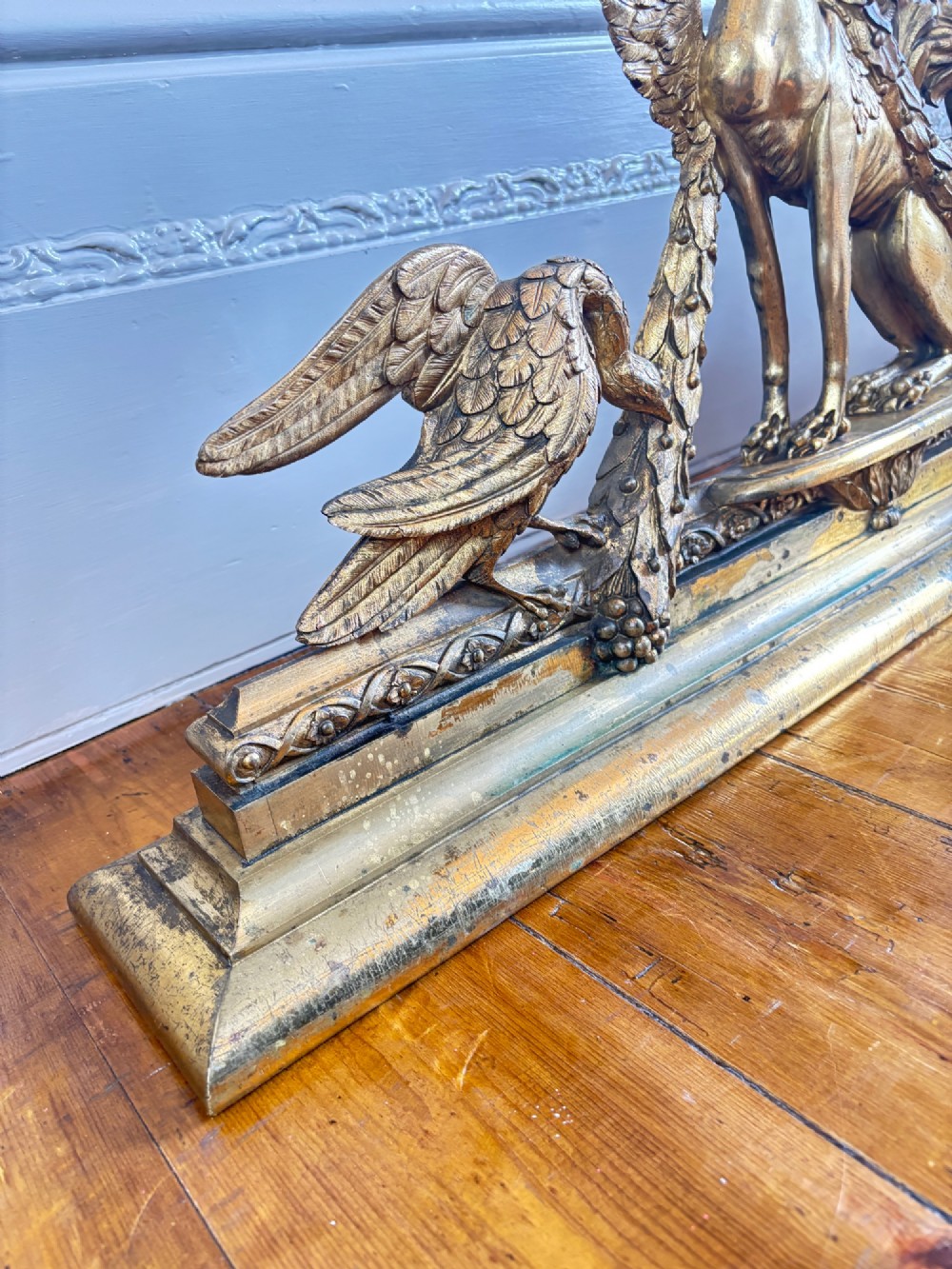 A long gilt bronze fireplace fender featuring winged sphinxes on either side, foliate scrollwork, and a central classical urn on a stepped base. View VII