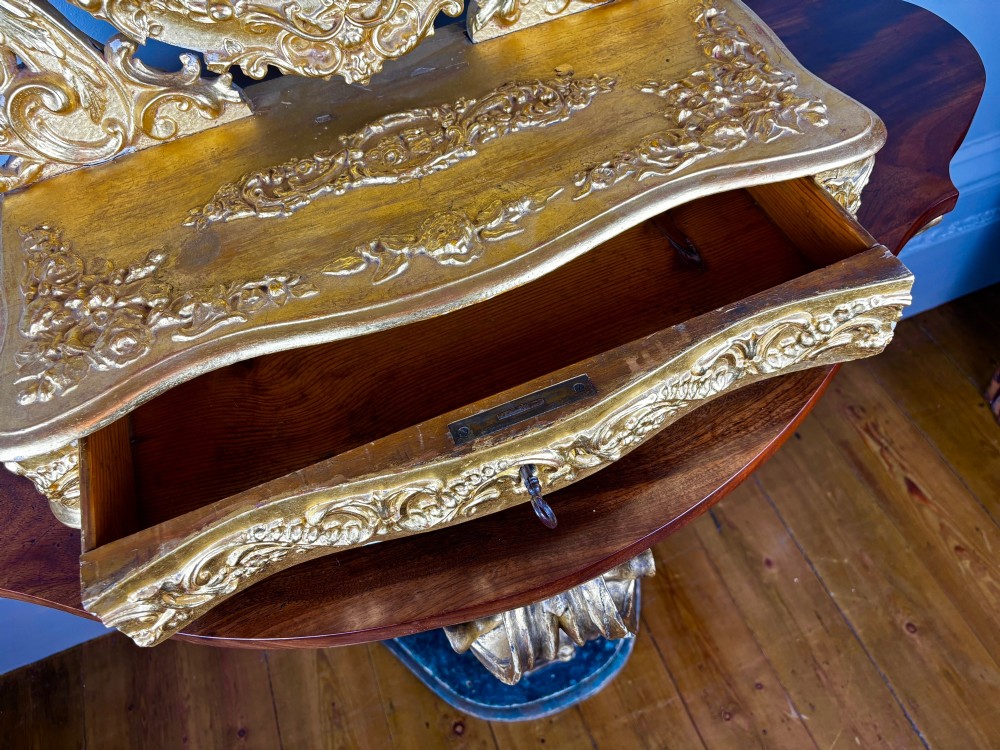 An 18th-century Italian giltwood table mirror featuring an oval glass frame supported by ornate scroll carved arms atop a single-drawer plinth base. View III