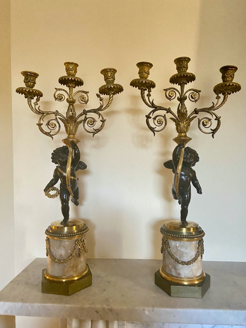 A pair of late Louis XVI style candelabra featuring dark patinated bronze putti holding multi-arm gilt bronze candle holders, mounted on circular fluorspar pedestals with ormolu floral swags.