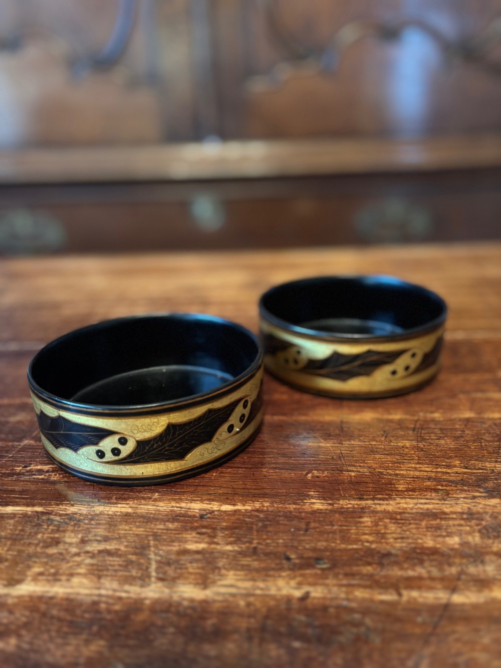 A pair of circular Regency black lacquered papier-mache wine coasters decorated with hand-painted gilded foliage motifs around the outer rim. View VI