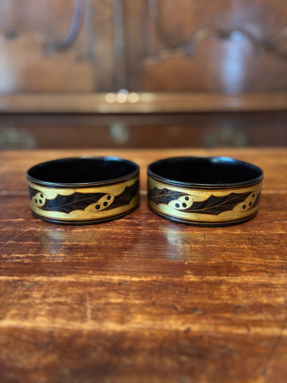 A pair of circular Regency black lacquered papier-mache wine coasters decorated with hand-painted gilded foliage motifs around the outer rim. View VII